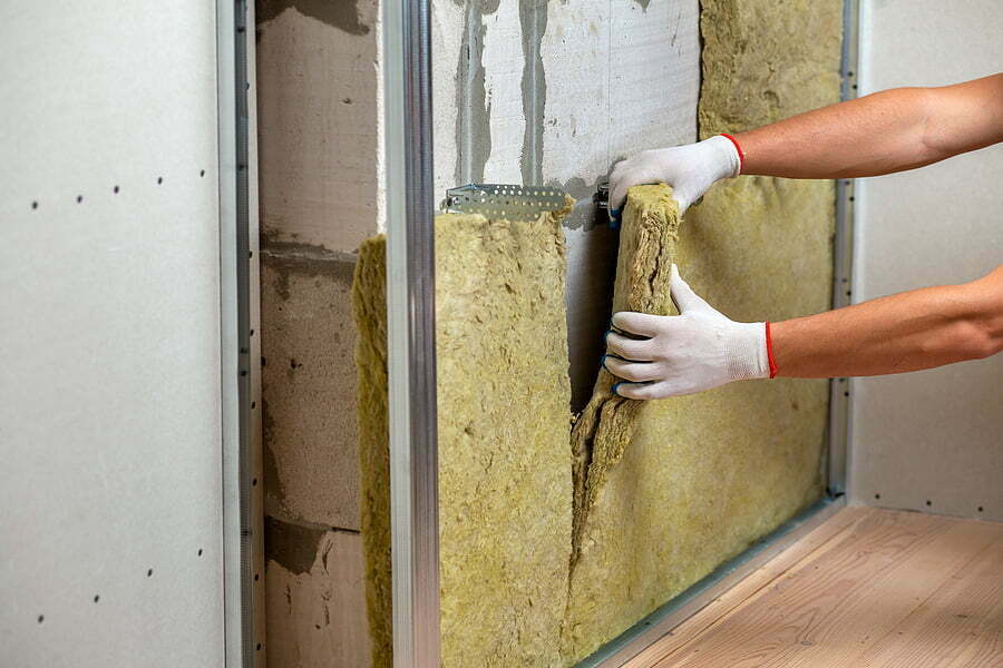 worker insulating a room wall with mineral rock wool thermal insulation.